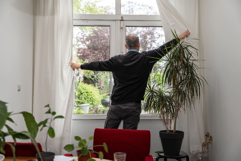 man voor raam opent gordijnen